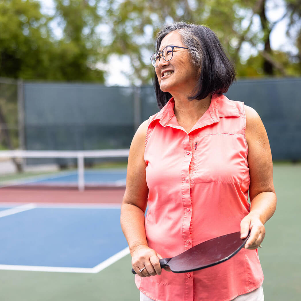 A woman stands with a pickleball paddle.