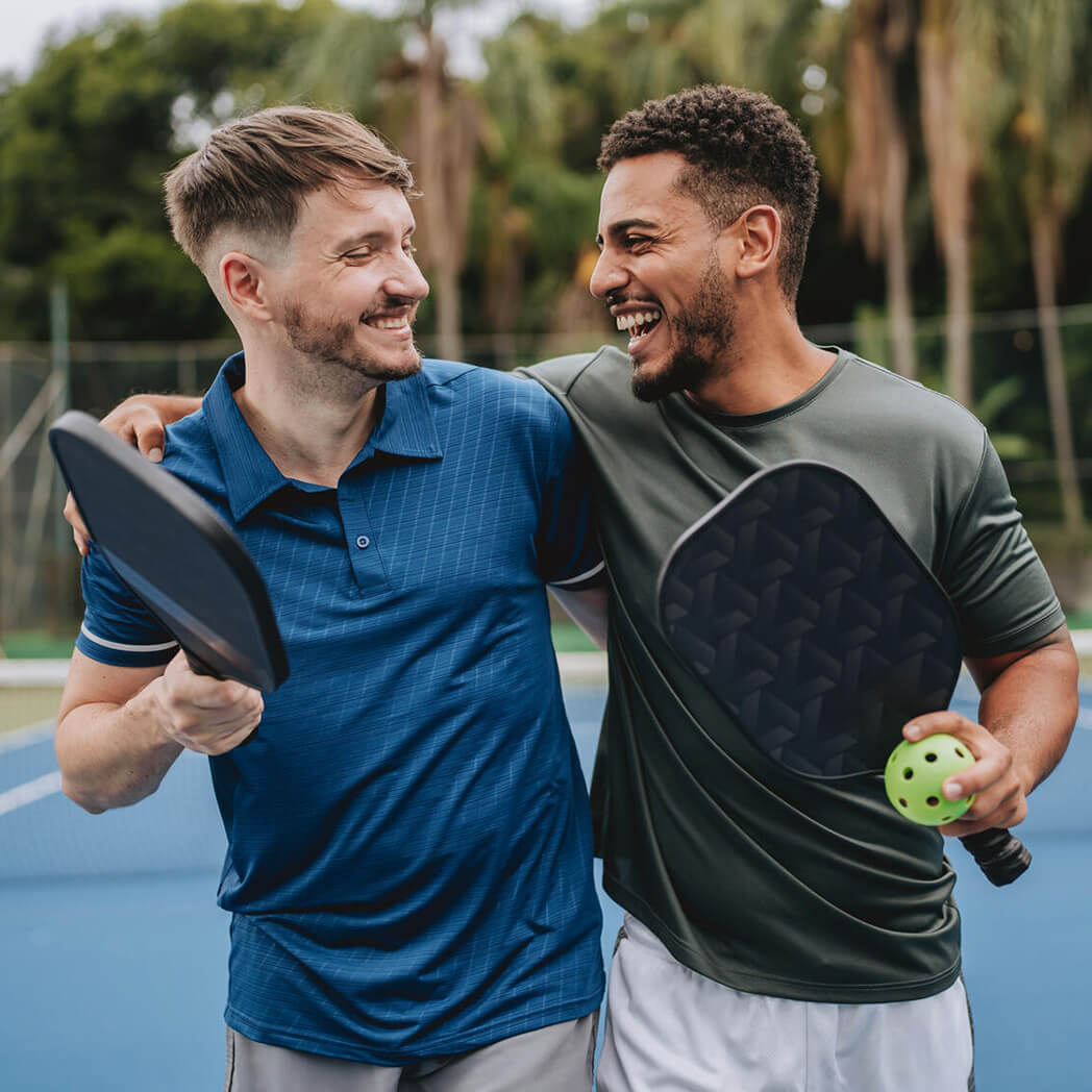 Two smiling men walking to the baseline of a pickleball court.